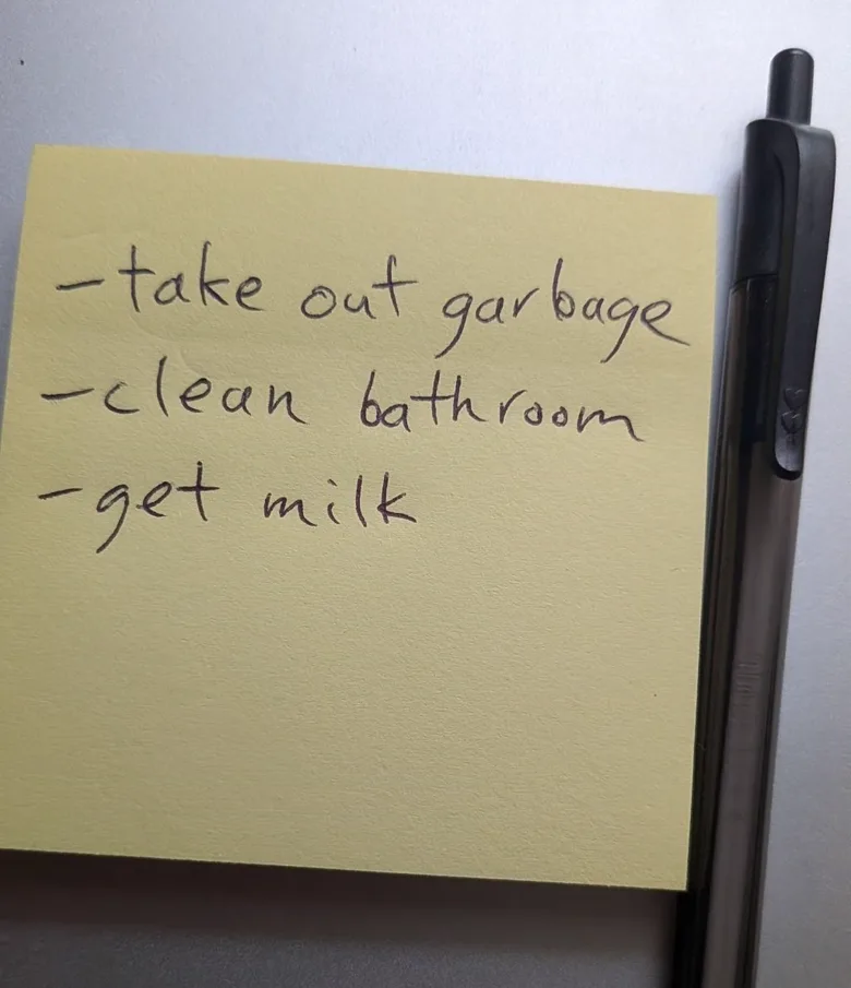 A yellow sticky note beside a pen, handwritten: take out garbage, clean bathroom, get milk